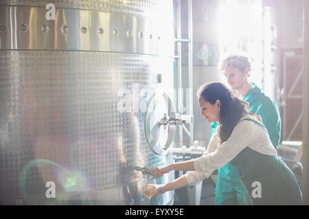 Vintners barrel tasting white wine from stainless steel vat in sunny cellar Stock Photo