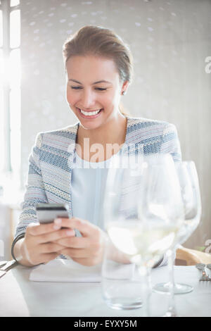 Smiling woman texting with cell phone at restaurant table Stock Photo