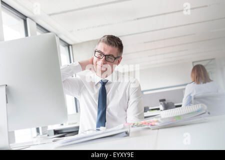 Businessman rubbing neck at computer in office Stock Photo