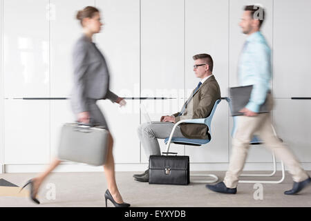Businessman working at laptop in lobby behind business people on the move Stock Photo