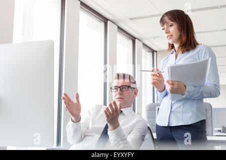 Businessman at computer gesturing and explaining to businesswoman in office Stock Photo