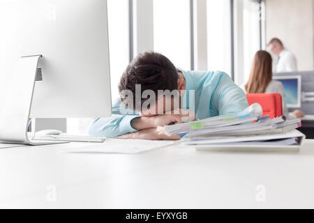 Frustrated businessman with head down next to stack of reports on desk Stock Photo