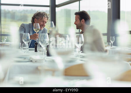 Men toasting wine glasses at restaurant table Stock Photo