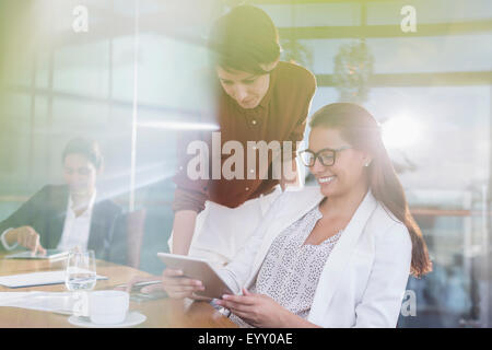 Businesswomen using digital tablet in sunny conference room Stock Photo