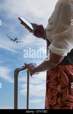 Chinese traveler using cell phone under airplane in blue sky Stock Photo