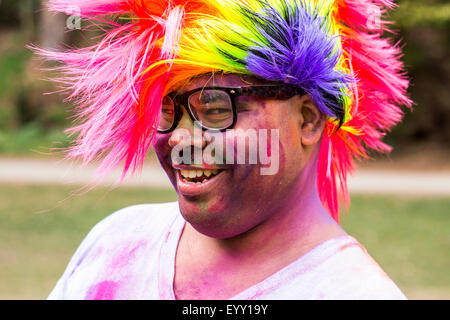 Smiling man covered in pigment powder wearing multicolor wig