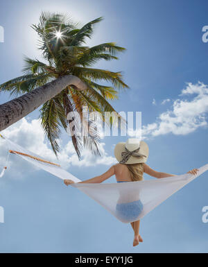 Caucasian woman sitting in hammock under palm tree Stock Photo
