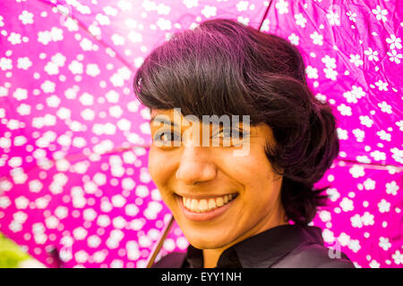 Smiling Hispanic woman holding pink umbrella
