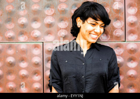 Hispanic woman smiling near metal wall Stock Photo