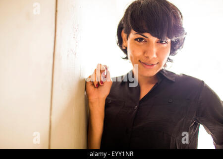 Smiling Hispanic woman leaning on wall Stock Photo