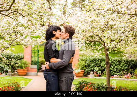 Couple kissing under flowering trees in park Stock Photo