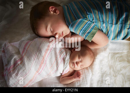 Boy napping with newborn sibling on bed Stock Photo