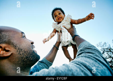 Black father holding baby daughter under blue sky Stock Photo