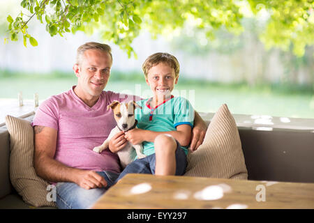 Caucasian father and son sitting with dog on sofa Stock Photo