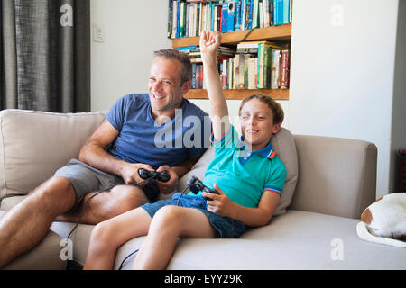 Caucasian father and son playing video games on sofa Stock Photo