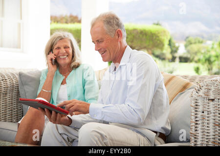 Caucasian couple using cell phone and digital tablet on sofa Stock Photo