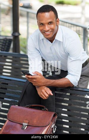 Black businessman using cell phone on park bench Stock Photo