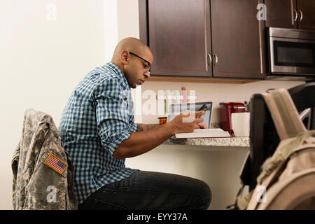 Mixed race soldier using laptop and cell phone on counter Stock Photo