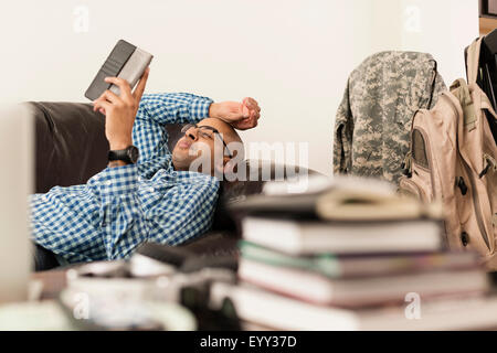 Mixed race man using digital tablet on sofa near books Stock Photo