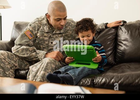 Mixed race soldier father and son using digital tablet on sofa Stock Photo
