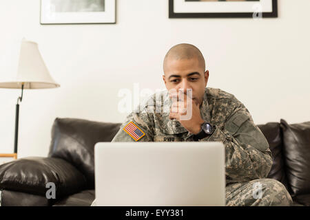 Mixed race soldier using laptop on living room sofa Stock Photo