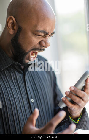 Frustrated black man using cell phone near window Stock Photo