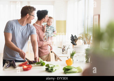 Caucasian gay fathers and baby cooking in kitchen Stock Photo