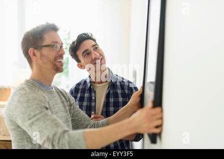 Caucasian gay couple hanging picture on wall Stock Photo