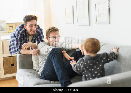 Caucasian gay fathers and baby relaxing on sofa Stock Photo