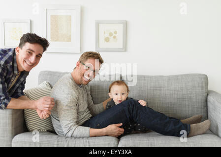 Caucasian gay fathers and baby relaxing on sofa Stock Photo