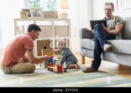 Caucasian gay fathers and baby relaxing in living room Stock Photo