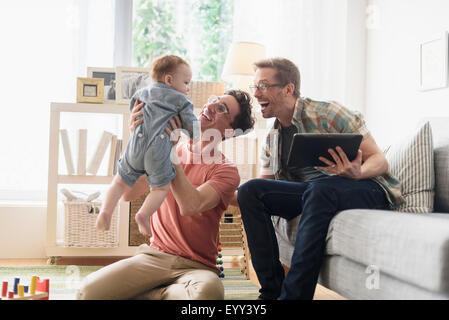 Caucasian gay fathers and baby relaxing in living room Stock Photo