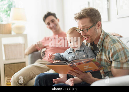 Caucasian gay fathers reading to baby in living room Stock Photo