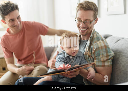 Caucasian gay fathers reading to baby in living room Stock Photo