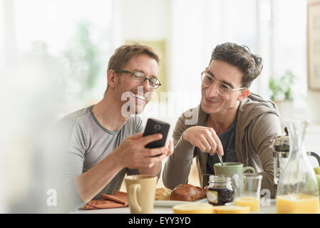 Caucasian gay couple using cell phone at breakfast Stock Photo