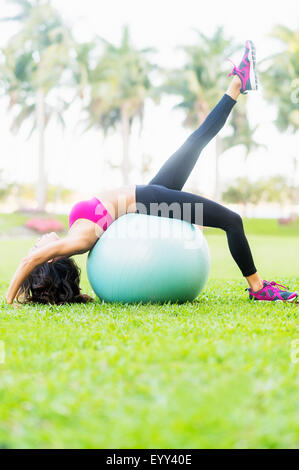 Chinese woman stretching on fitness ball in park Stock Photo