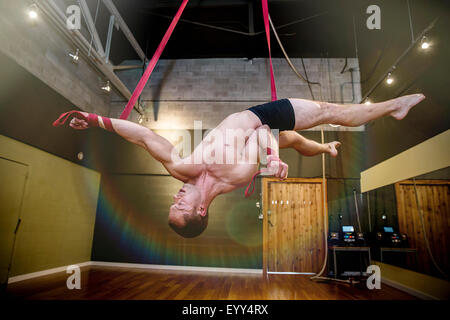 Caucasian acrobat hanging from ropes in studio Stock Photo
