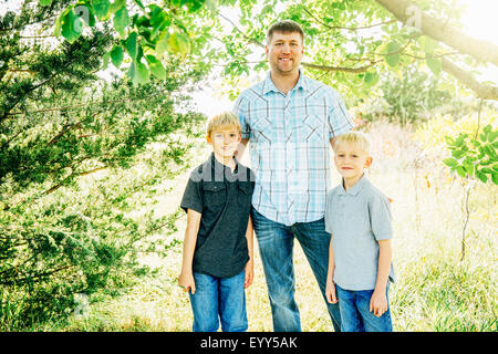 Caucasian father and sons smiling under trees Stock Photo