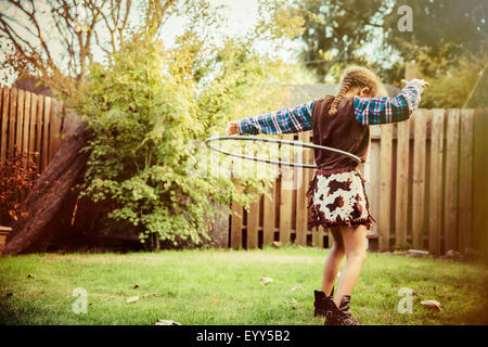 Mixed race girl in cowboy costume spinning plastic hoop in backyard Stock Photo