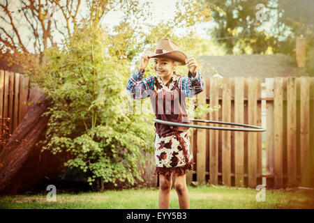 Mixed race girl in cowboy costume spinning plastic hoop in backyard Stock Photo