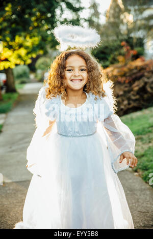 Mixed race girl wearing angel costume on sidewalk Stock Photo