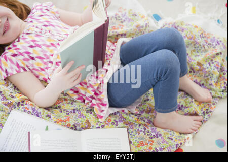 Caucasian girl reading book on bed Stock Photo