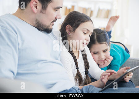 Caucasian father and daughters using digital tablet on sofa Stock Photo