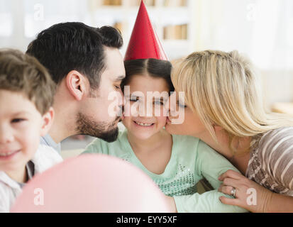 Caucasian parents kissing daughter at birthday party Stock Photo