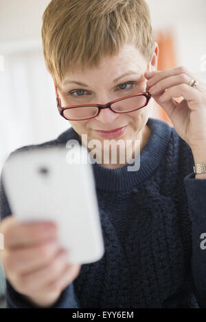 Caucasian woman peering over eyeglasses at cell phone Stock Photo