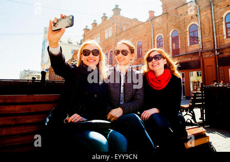 Caucasian women taking cell phone photographs on city bench Stock Photo