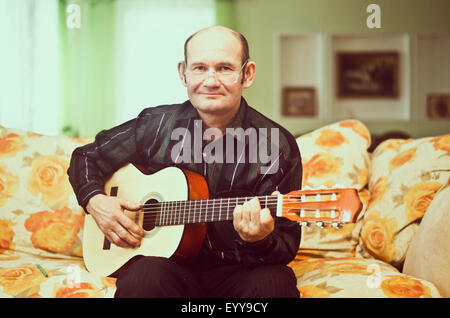 Caucasian man playing guitar on sofa