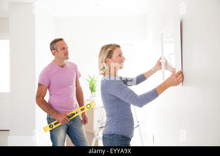 Caucasian couple hanging picture in new home Stock Photo