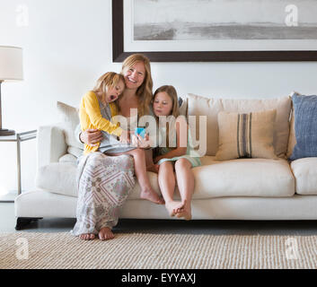 Caucasian mother and daughters using cell phone on sofa Stock Photo