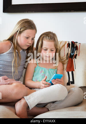 Caucasian girls using cell phone on sofa Stock Photo